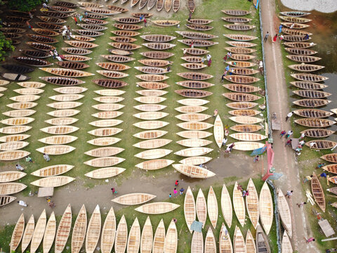 Manikganj, Dhaka Division, Bangladesh - 25 August 2021: Aerial view of Bost Market, featuring hundreds of traditional wooden boats arranged in rows on the grassy riverbank with people.