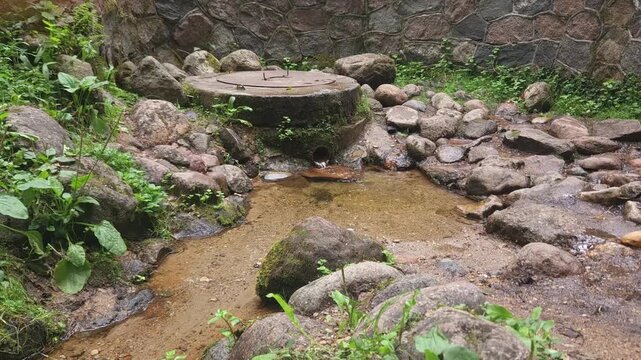 Stone water well surrounded by rocks and greenery in a natural setting  