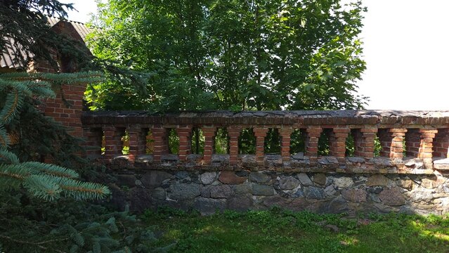 Old stone fence with brick balusters surrounded by greenery  