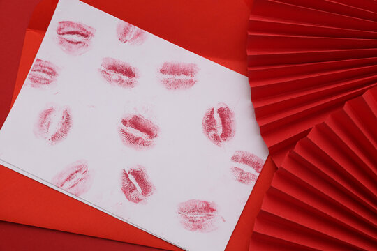 Lipstick kiss letter with red handmade paper fans on a red background. Valentine's Day.