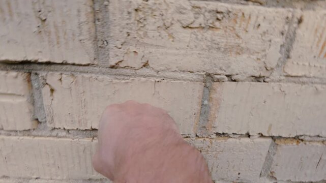 A man&rsquo;s fist strikes a brick wall. The guy is pounding his fists against the stone wall of the building without gloves. The fist is making contact with the bricks. From the first person.
