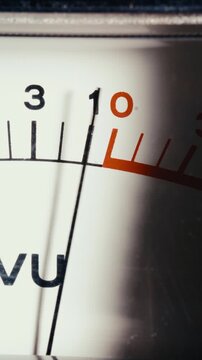 Analog volume unit level indicator display with needle peaking into red zone, measuring high audio signal decibels. Macro vertical shot