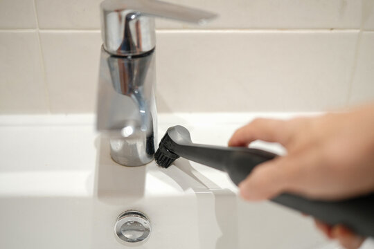 Woman cleaning bathroom sink faucet with small brush. Home hygiene and maintenance. Everyday domestic chore concept.