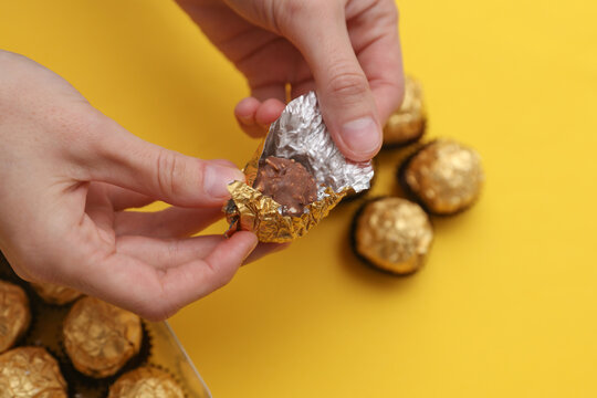 Hand holding Chocolate candy balls wrapped in gold foil on yellow background