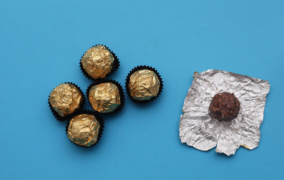 Chocolate candy balls wrapped in gold foil on blue background