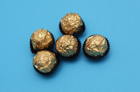 Chocolate candy balls wrapped in gold foil on blue background