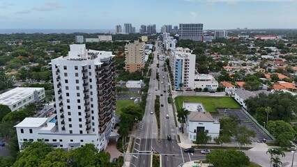 Fototapeta premium Aerial view of a modern white residential high rise tower beside a wide palm lined boulevard in a Miami neighborhood with the Atlantic Ocean on the horizon