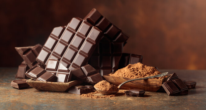 Scraps of dark chocolate next to a wooden bowl of cocoa powder.