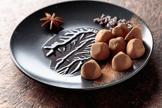 Chocolate truffles on a black plate with chocolate sauce.