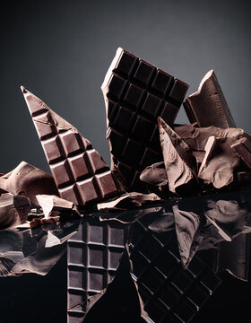 Big hunk of dark bitter chocolate and broken chocolate bars on a black reflective background.