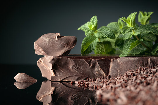 Pieces of dark bitter chocolate and chocolate chips with mint on a black reflective background.