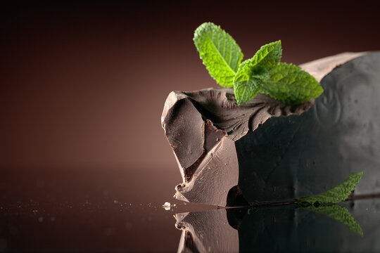 Large piece of dark bitter chocolate with mint on a black reflective background.