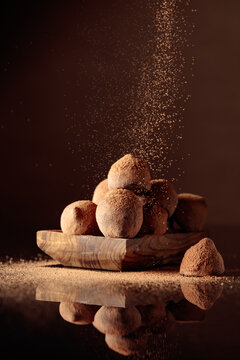 Chocolate truffles in small wooden dish sprinkled with cocoa powder. Black reflective background.