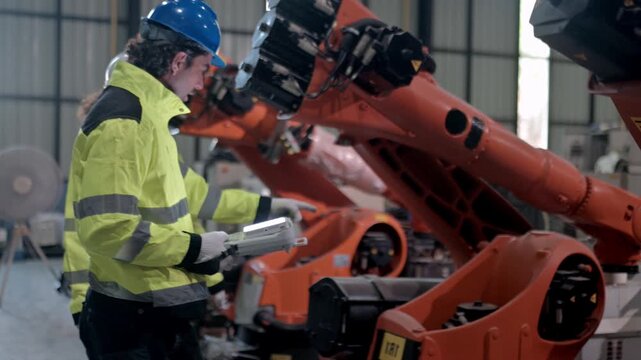 Industrial Automation: A worker in a hard hat and high-visibility jacket inspects a row of robotic arms on an assembly line, showcasing the synergy between human expertise and automated manufacturing.