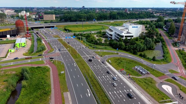 High angle aerial drone video clip of multi-lane highway overpass bridge with vehicle traffic, bike path, parking lot, corporate Ecolab building, and construction crane in Netherlands, West Europe