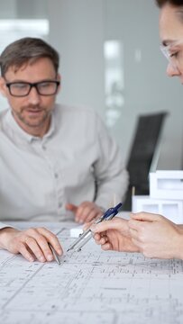 Architects are teamwork planning a building design project, reviewing detailed blueprints with a compass and a ruler, working on technical drawings and a digital tablet at the office, close up