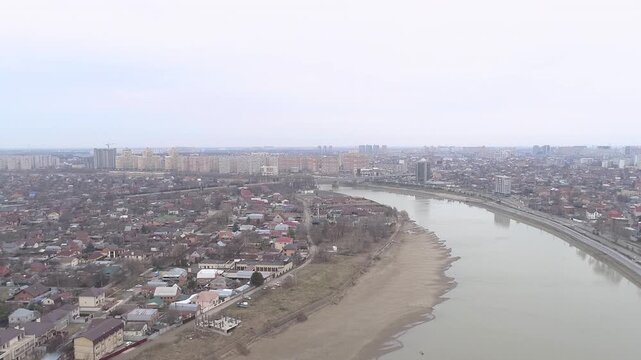 An aerial shot of a suburban area in Krasnodar  showcasing a mix of residential buildings  a river  and surrounding greenery under a cloudy sky.