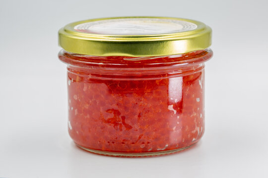 Glass jar of red caviar on a white background, closeup.