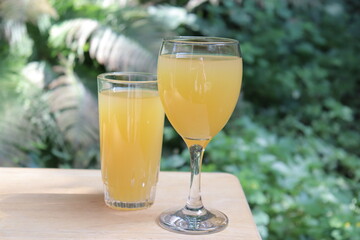 Glasses of orange juice on a wood table in the garden. Fruit juice in summer with a green background and vegetation. Refreshment and natural juice in orange color. © Martine