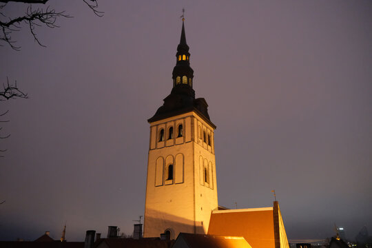 illuminated St. Nicholas Church (Niguliste Church) tower and spire at night in Tallinn Old Town.