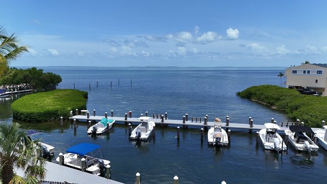 Aerial view of a wooden dock with moored motorboats and mangrove islands on the calm turquoise water of the Florida Keys under a blue summer sky