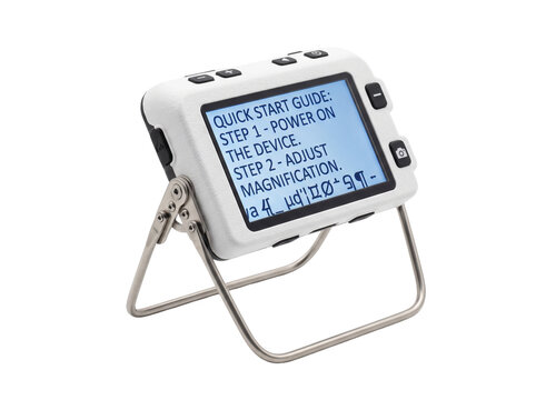 Digital electronic magnifier low vision aid reader device displaying quick start text guide on foldable metal stand for visual impairment accessibility and senior eye care assistance. Isolated black.
