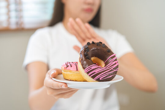 Diet concept, asian young woman hand push out, deny sugar donut, doughnut and sweet taste food on plate, fighting to keep it from getting fat when person bring to me. Healthy nutrition of weight loss.