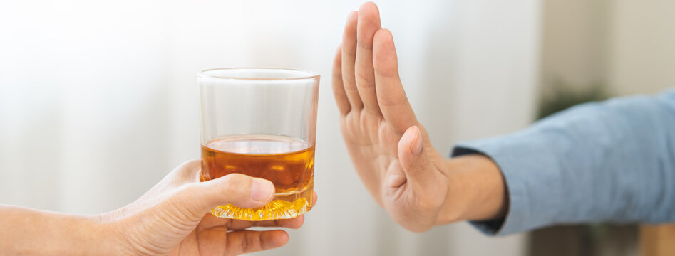 Close up of Asian young man making stop hand gesture to refuse a glass of whiskey, responsible man saying no to alcohol drink, stop alcoholism and addiction social problem, health care concept