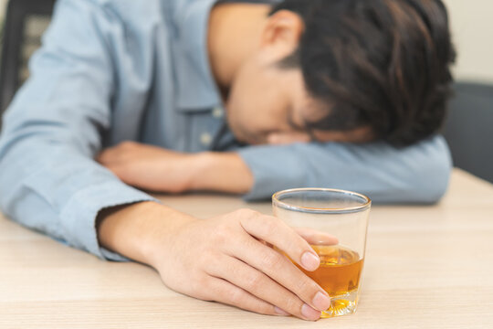 Health care alcoholism drunk, fatigue asian young man hand holding glass of whiskey, alone depressed male drink booze on sofa at home. Treatment of alcohol addiction, suffer abuse problem alcoholism.