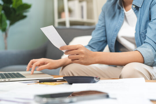 Close up of a person hand holding receipts while using laptop and calculator for home budget planning, financial management, monthly expense tracking and tax calculation