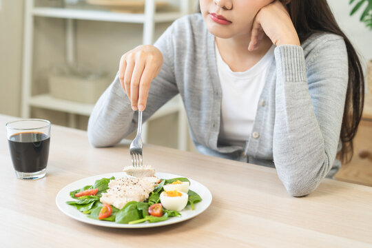 Diet bored concept, unhappy asian young woman, girl on dieting, holding fork at chicken breast on salad plate, dislike or tired with eat fresh vegetables. Nutrition of clean, healthy food good taste.