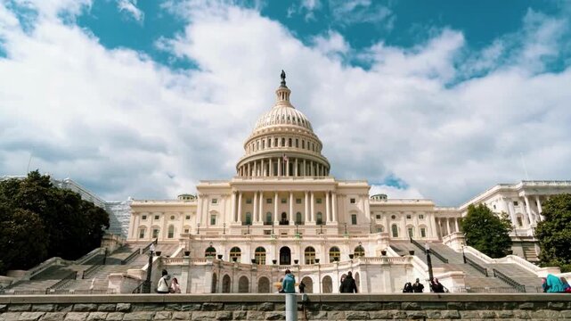 Low angle wide shot of united states capitol building in washington dc with people walking on stairs during bright sunny day blue sky and clouds movement.