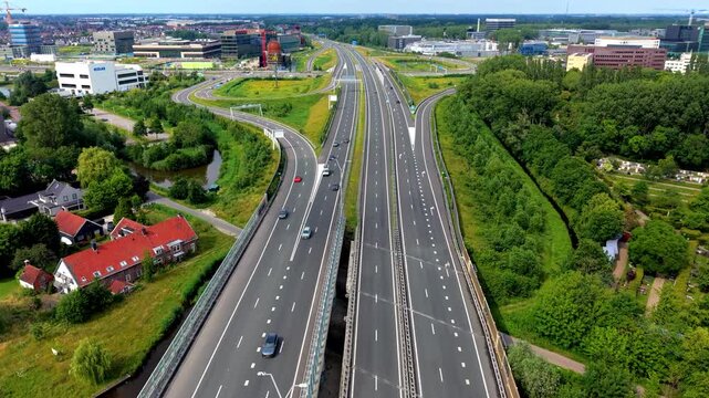 High angle aerial drone video clip of multi-lane highway interchange with driving cars, bike path, car parking lot, Ecolab building, and corporate office parks in Netherlands, West Europe