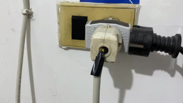 An old white interior wall featuring a triple power outlet setup with two plugs actively connected and the third unused socket sealed over with heavy-duty gaffer tape inside a room.