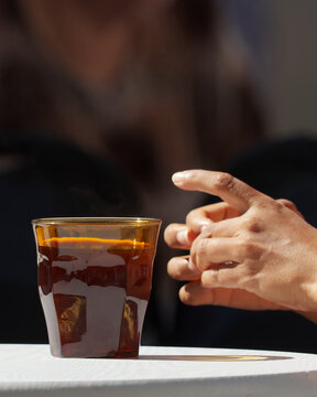 Close-up vertical crop of a hand reaching for a glass of chilled amber drink on a white table, blurred background above offers copy space for mobile and social media designs.