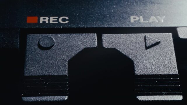 Finger pressing record button on vintage audio deck with REC and PLAY written above plastic controls. Macro shot