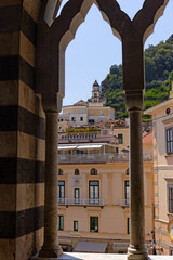 Pionowy kadr przedstawiający malowniczy widok na miasteczko Amalfi na Wybrzeżu Amalfi, region Kampania, Włochy, sfotografowany przez zabytkowe, przeplatane łuki krużganków Katedry Św. Andrzeja © Grzegorz
