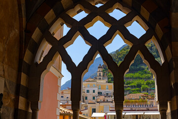 Malowniczy widok na miasteczko Amalfi na Wybrzeżu Amalfi, region Kampania, Włochy, sfotografowany przez zabytkowe, przeplatane łuki arabsko-normandzkie krużganków Katedry św. Andrzeja © Grzegorz