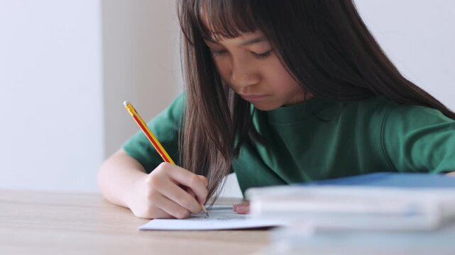 Selective focus portrait of an Asian kid improving her writing skills. The young student is focused on her textbook assignment, representing homeschooling, diligent study, and modern education.