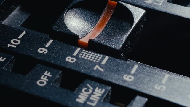 Finger adjusting slider control on retro audio mixing panel with numbered level markings. Extreme close-up shot