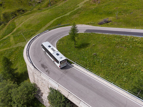Rocca Pietore, Veneto, Italy - 15 August 2026: Aerial view of a bus navigating a sharp hairpin bend on the mountain road of Passo Fedaia, surrounded by green alpine slopes.