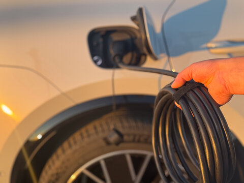 Hand holding a coiled charging cable beside an electric car wheel at sunset, ready for vehicle charging porsche macan 4 electric Poland, Pszczyna, 3.08.2026
