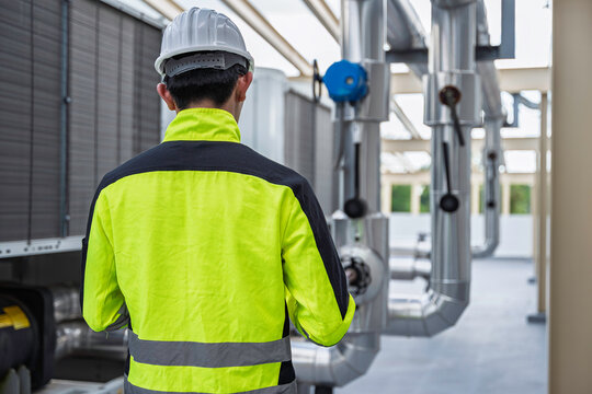 Industrial engineer inspects cooling water pipes at a large industrial facility. Concept of cooling system, engineering, thermal management, utilities, infrastructure, and plant operations.