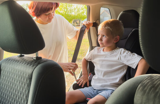 woman securing child in car seat with white shirt and blue shorts, careful and attentive in car interior, daytime side view, family safety, child transportation, fabric, plastic, metal, day.