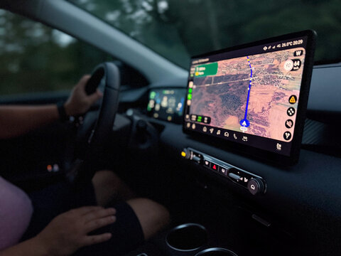 Driver using a digital navigation screen inside a car at dusk, with a lit map guiding the route during a road trip