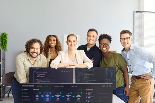 Developers team programmers in office startup coding. Smiling colleagues behind monitors with code present a group portrait for tech marketing and recruitment. Strong concept of team success.