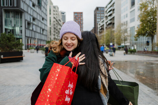 Friends hugging after christmas winter shopping in city
