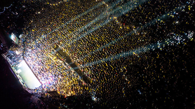 Dhaka, Bangladesh - 28 November 2022: Aerial view of a massive crowd gathered at an outdoor event illuminated by bright stage lights at night.