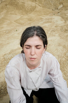 Girl sits on sand with eyes closed in nature during the day