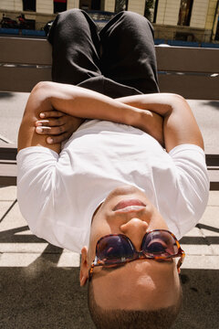 Man lying upside down on bench in sunglasses editorial